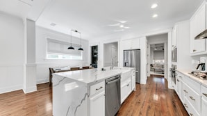 A modern kitchen with a marble island, stainless steel appliances, and wooden flooring.