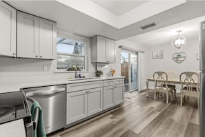 A modern kitchen with white cabinetry, a built-in dishwasher, and a dining area with a table and chairs. - 4BR | Screened Pool | Next to Park | 10 Min Indian Rocks Beach | Sleeps 10 (Largo)