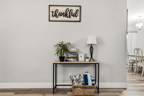 A room with a wall-mounted sign reading 'thankful,' a small table with a lamp, a plant, and books. - 4BR | Screened Pool | Next to Park | 10 Min Indian Rocks Beach | Sleeps 10 (Largo)