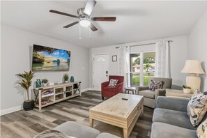 A living room with a ceiling fan, a television, a sofa, a coffee table, and a window with curtains. - 4BR | Screened Pool | Next to Park | 10 Min Indian Rocks Beach | Sleeps 10 (Largo)