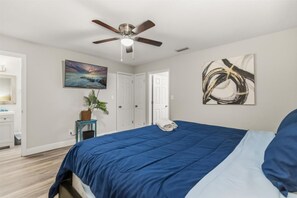 A bedroom with a bed, ceiling fan, artwork, and a plant. - 4BR | Screened Pool | Next to Park | 10 Min Indian Rocks Beach | Sleeps 10 (Largo)