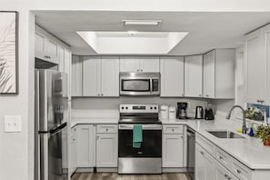 A modern kitchen with white cabinets, stainless steel appliances, a skylight, and a sink with a plant.