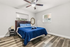 A bedroom with a bed, a nightstand, a ceiling fan, and two windows with blinds. - 4BR | Screened Pool | Next to Park | 10 Min Indian Rocks Beach | Sleeps 10 (Largo)