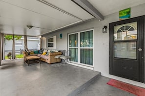 A covered porch with a sofa and chairs, a black door with a window, and a welcome sign. - 4BR | Screened Pool | Next to Park | 10 Min Indian Rocks Beach | Sleeps 10 (Largo)