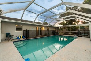 A covered swimming pool with a glass ceiling, a slide, and a fenced area. - 4BR | Screened Pool | Next to Park | 10 Min Indian Rocks Beach | Sleeps 10 (Largo)