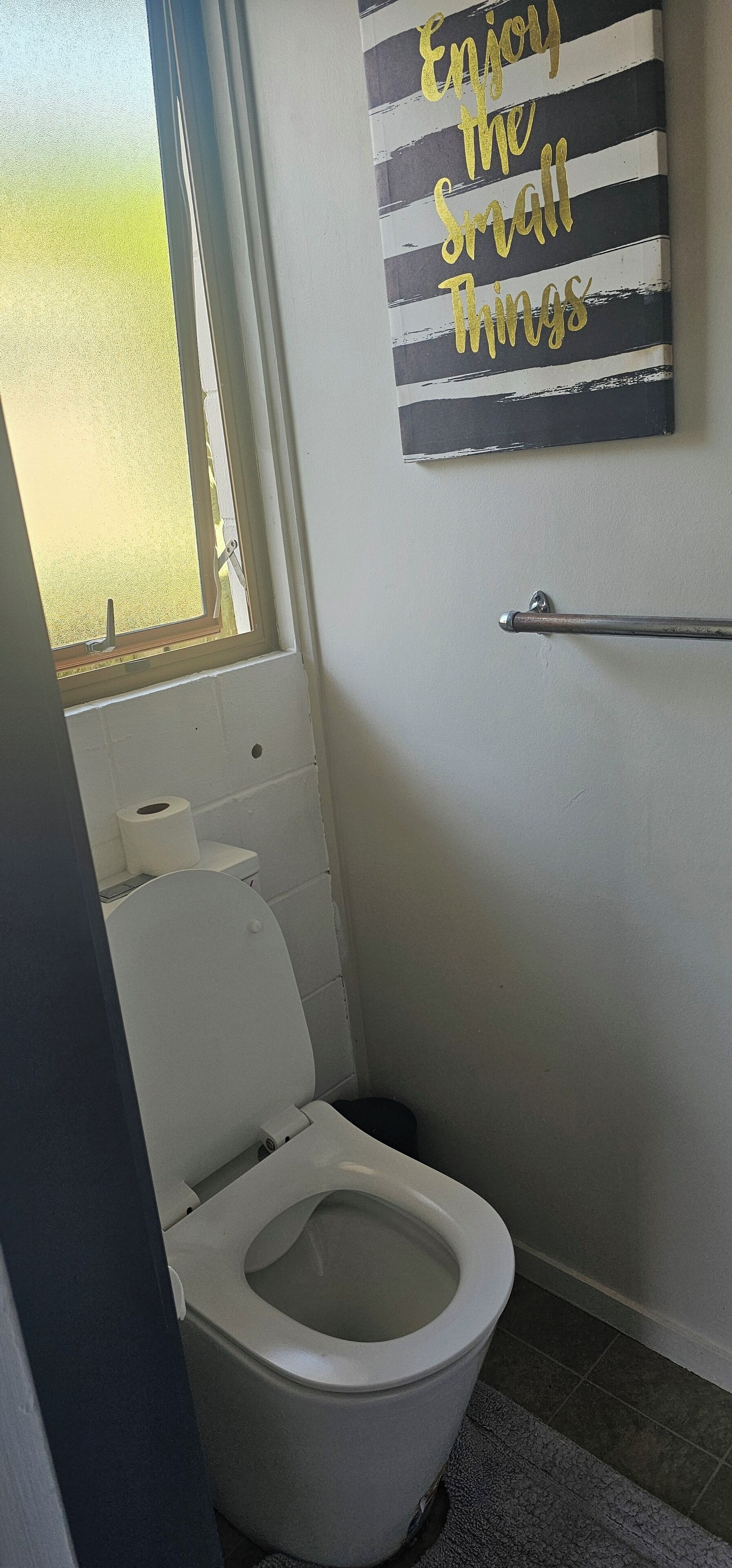 A small bathroom with a toilet, a window, and a motivational quote on the wall.