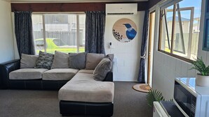 A cozy living room with a sectional sofa, a small table with a microwave, and a potted plant. - Cozy Cove Ohope Beach (Ohope)