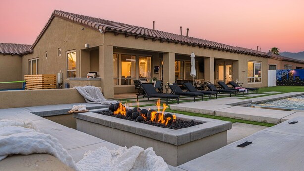 Ein modernes Haus mit Terrasse, Feuerstelle, Liegestühlen und Schwimmbecken.