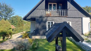 Una casa a due piani in legno con un balcone, un'antenna parabolica e un piccolo giardino.