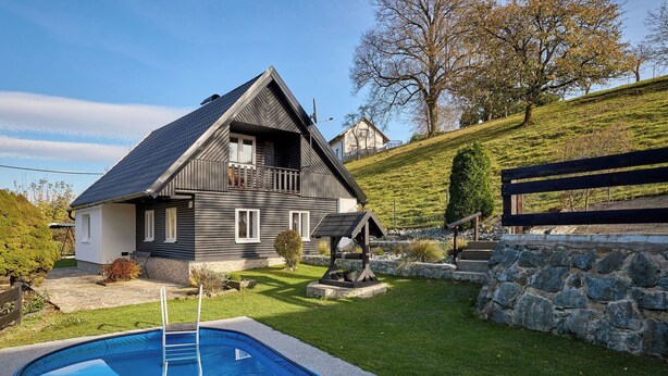 Una casa a due piani con piscina, un muro in pietra e una recinzione in legno.