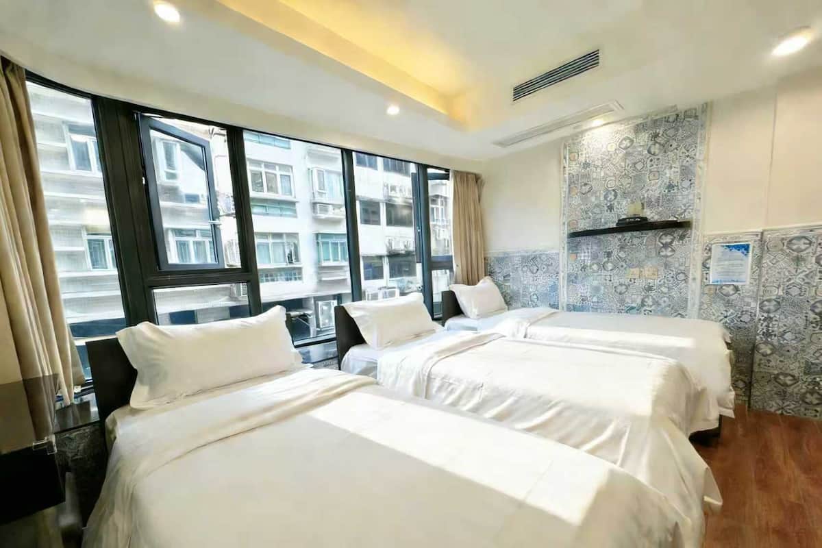 Een hotelkamer met drie bedden, grote ramen en een behang met patroon.