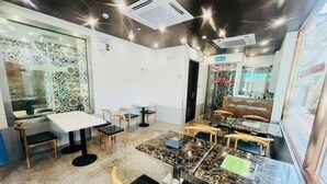 A restaurant with marble tables and wooden chairs, a tiled backsplash, and a glass partition. - Hou Kong Boutique Hostel (Macau)