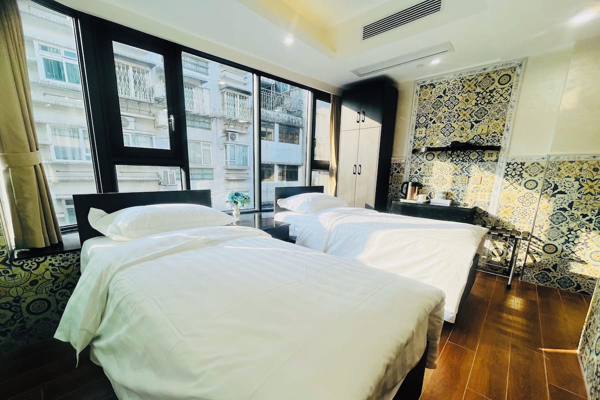 Een hotelkamer met twee bedden, een groot raam, een minibar en betegelde vloer.