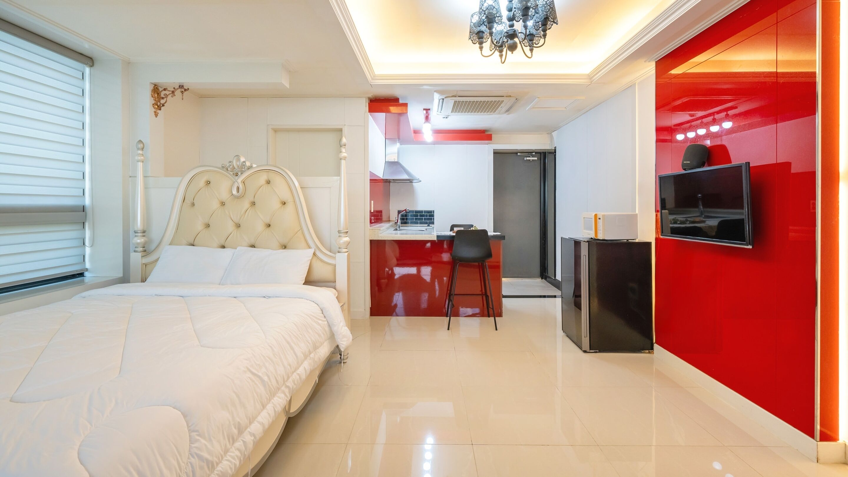 Una habitación de hotel moderna con una cama grande, kitchenette y televisor montado en la pared.