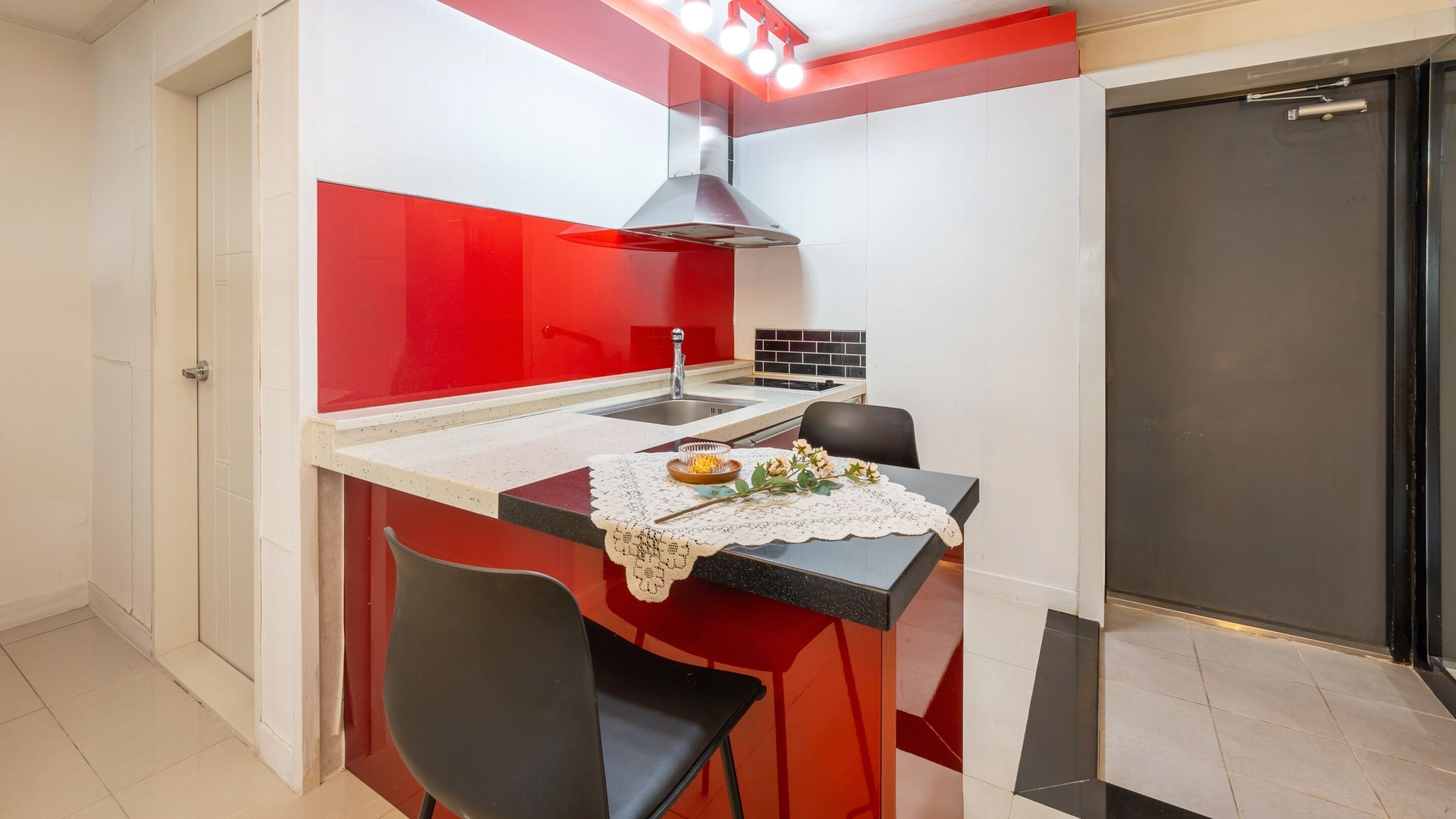 Une cuisine de taille réduite aux couleurs rouge et blanche, comprenant un évier, une cuisinière et un coin repas avec une chaise et une table.