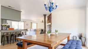 A modern kitchen with a wooden table and bar stools, a dining area with blue cushioned benches, and a chandelier.