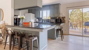 A modern kitchen with a large island, bar stools, and a view of the outdoor deck.