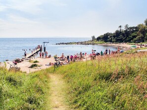Ein Strand mit felsigem Ufer, einer Holzsteganlage und Menschen, die das Wasser genießen.