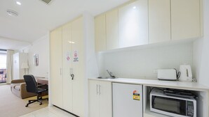 A compact kitchen with a microwave, kettle, and sink. There are cabinets and a chair visible. - MetaWise 2Bed Next to ICC Darling Harbour 65 (Sydney)