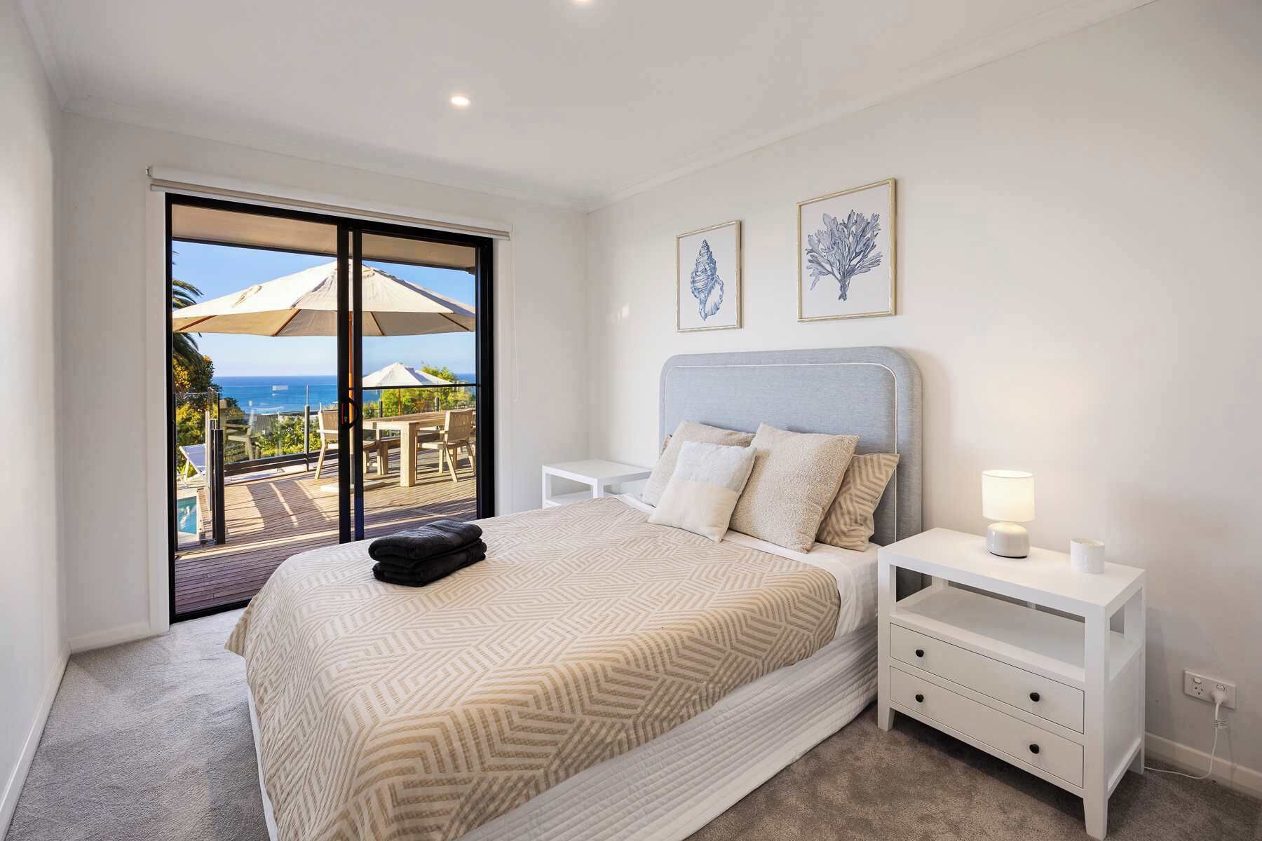 A bedroom with a bed, nightstands, a view of the ocean, and two framed artworks.