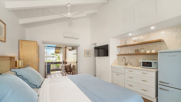 Un dormitorio con cama, ventilador de techo, kitchenette con microondas y puerta que da a un balcón.