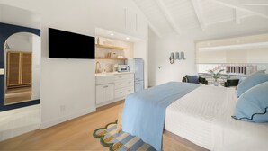 Un dormitorio moderno con una cama grande, un televisor en la pared, una zona de cocina y un balcón con vistas.