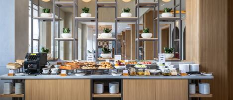 A buffet setup with various food items, a coffee machine, and multiple bowls of fruits and vegetables.
