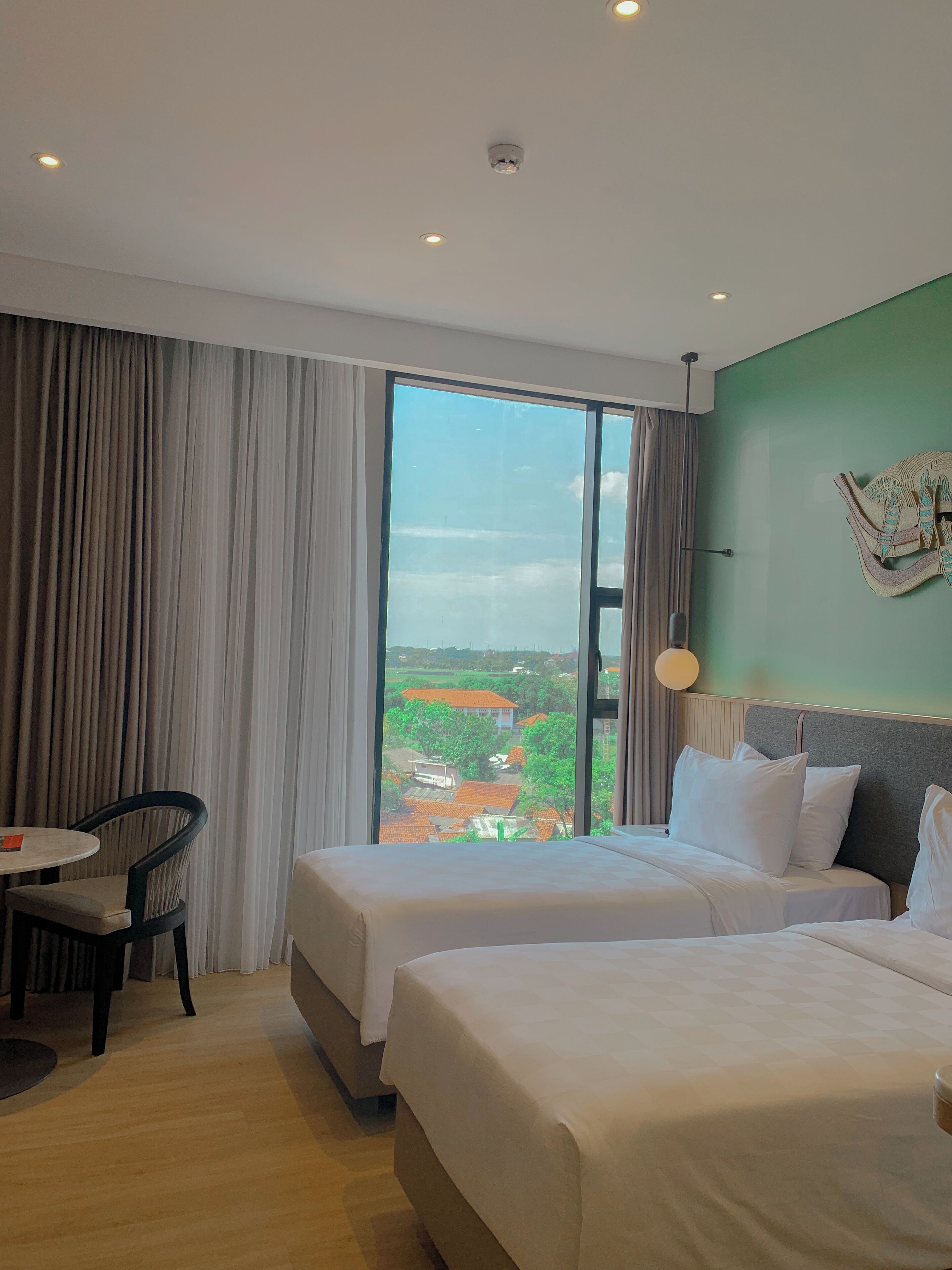 Habitación de hotel con dos camas, una mesa de comedor y vista a un paisaje verde.