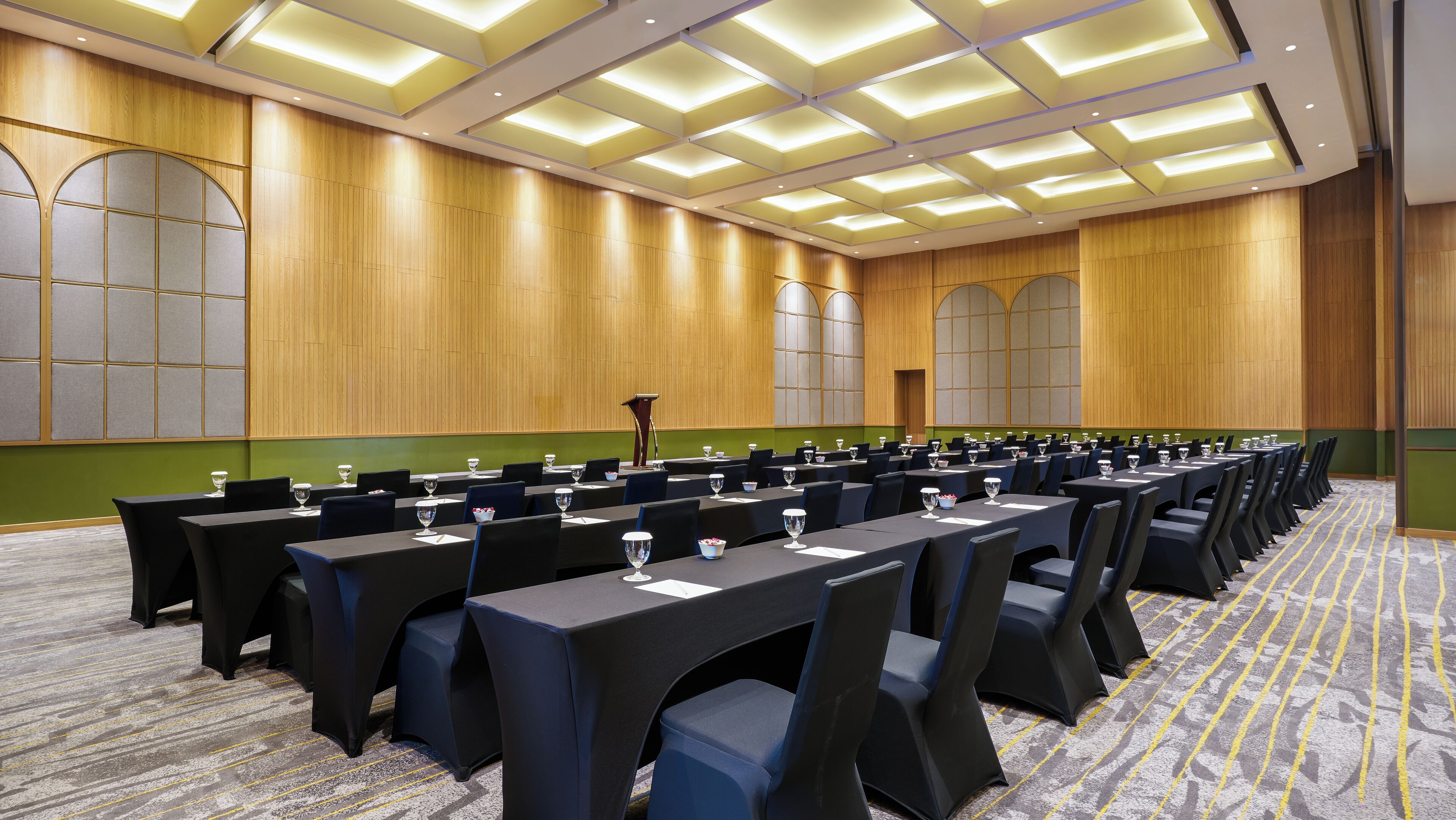 A conference room with long tables, chairs, and glassware, featuring wooden paneling and a green accent wall.