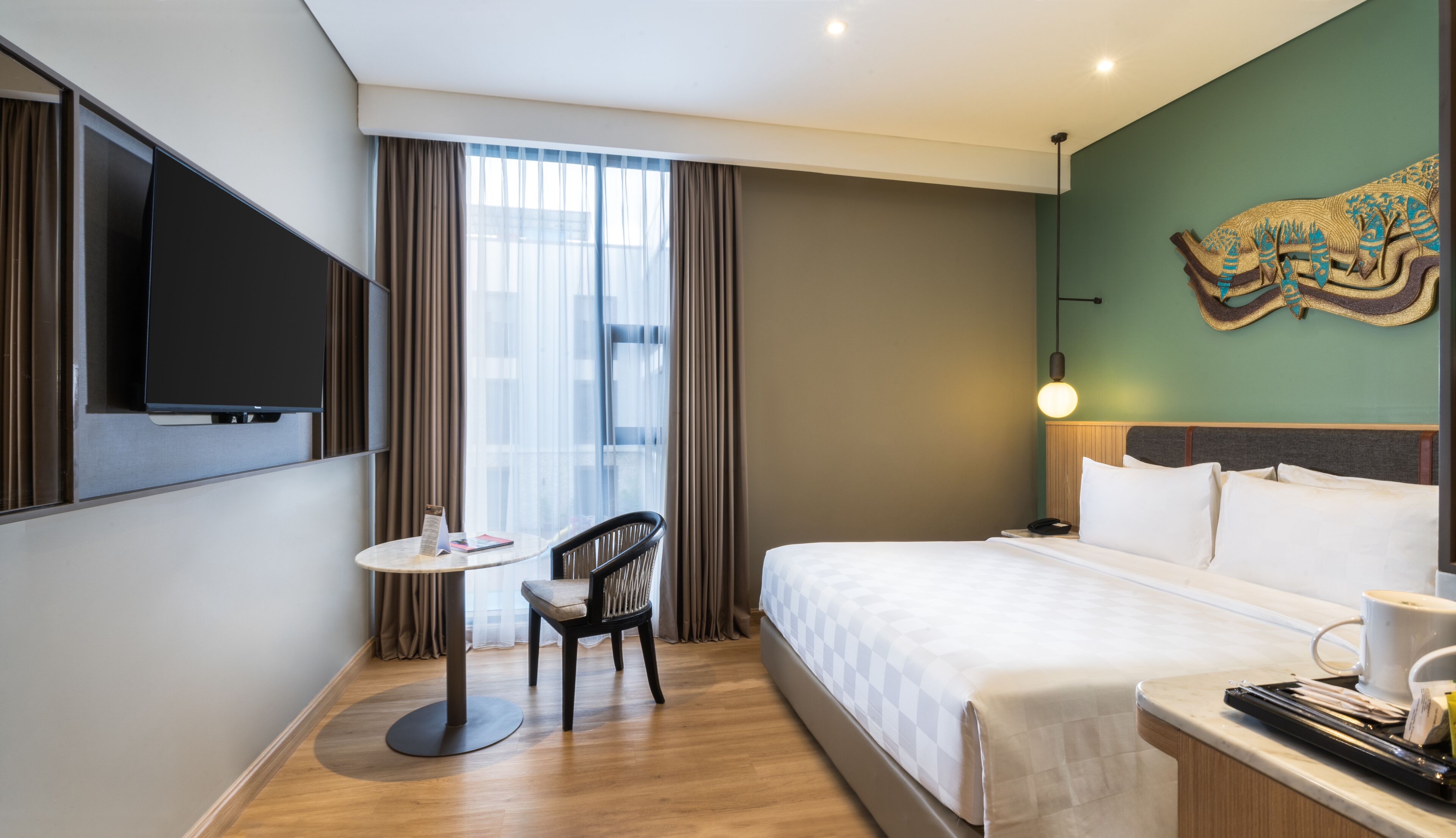 Habitación de hotel con cama, escritorio, silla, televisor y ventana con cortinas.