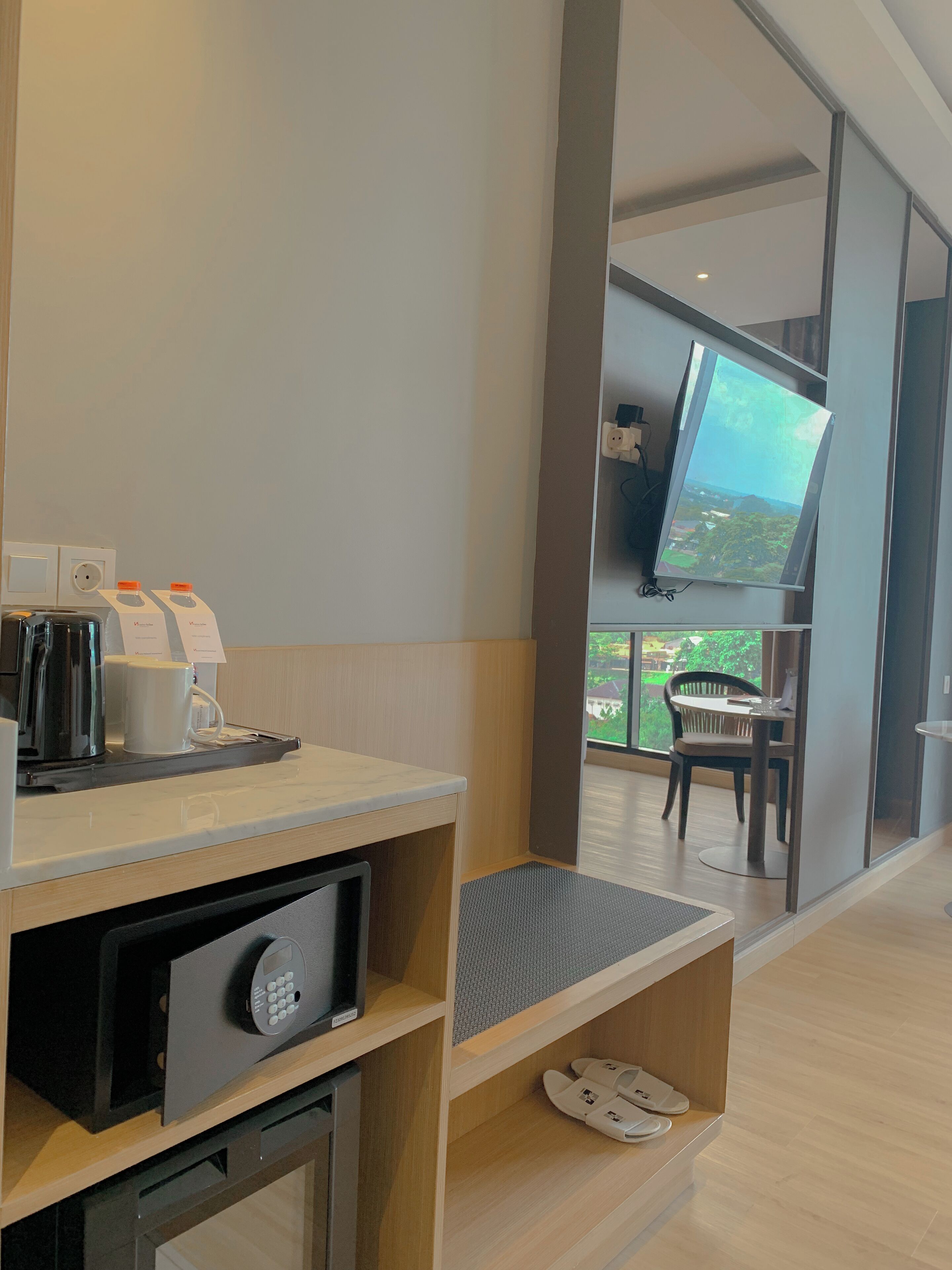 A modern hotel room with a coffee station, a television, and a view of the outdoors.