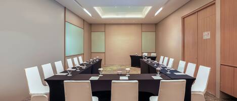 Een vergaderzaal met een lange tafel, witte stoelen en een vloerbedekking.