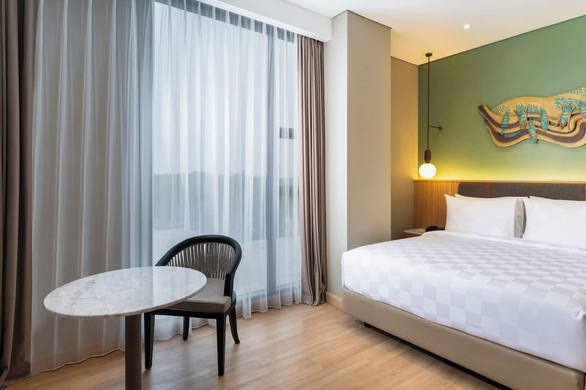 Ein Hotelzimmer mit einem großen Bett, einem kleinen runden Tisch, einem Stuhl und Blick durch transparente Vorhänge.