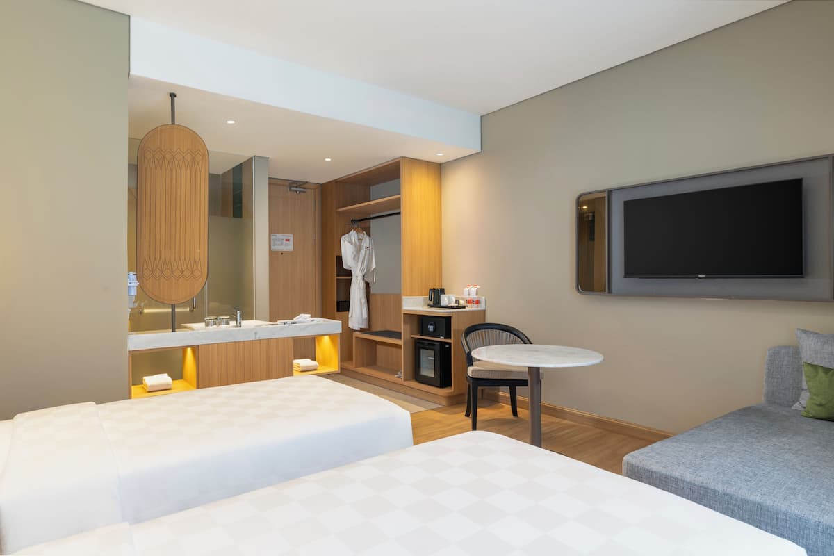 Ein Hotelzimmer mit zwei Betten, einem kleinen Tisch, einem Fernseher, einem Bademantel und einer Minibar.