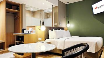 A hotel room with a bed, a desk with a computer, a chair, a round table, and a mirror.