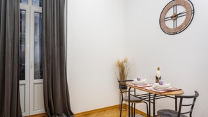 A dining area with a table set for two, a clock on the wall, and a window with curtains. - Lovely apartment in Rijeka with WiFi (Rijeka)