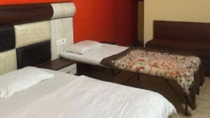 A hotel room with two single beds, a small table, and an air conditioning unit on the wall. - HR Rama Palace (Haridwar)