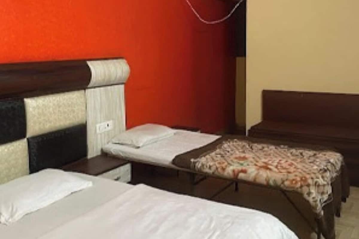 A hotel room with two single beds, a small table, and an air conditioning unit on the wall.