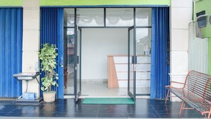 A hotel entrance with a glass door, a bench, and a potted plant. - Hotel O Ilir Timur I Near Rsud Siti Fatimah Az-Zahra Formerly Lumendiva Suite (Palembang)