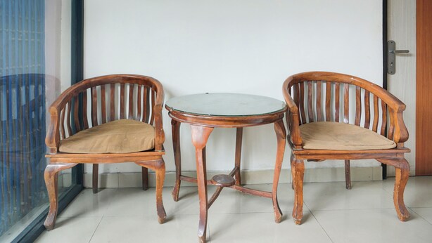 Two wooden chairs with cushioned seats and a small round table in between, positioned against a white wall with a door to the right. - Hotel O Ilir Timur I Near Rsud Siti Fatimah Az-Zahra Formerly Lumendiva Suite (Palembang)