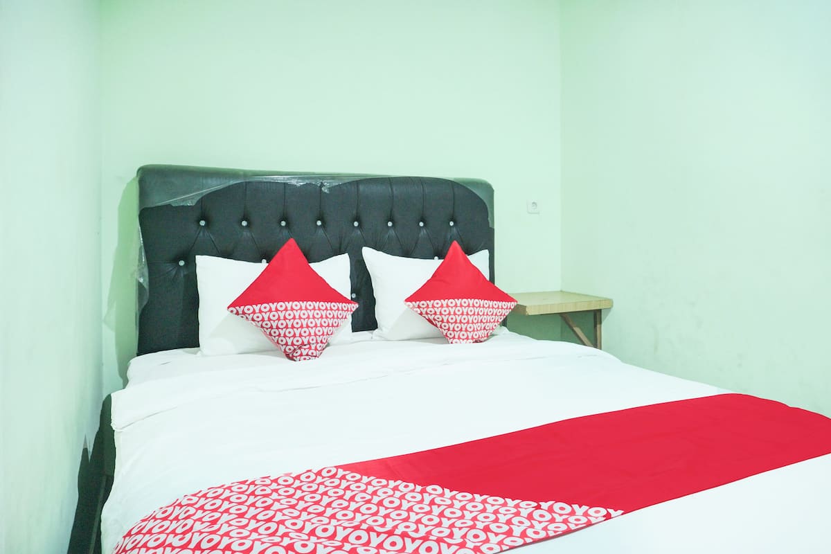 A bed with a dark headboard, white bedding, and red and white patterned pillows.