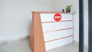 A reception desk with a wooden finish and a white panel featuring horizontal stripes and a red logo. - Hotel O Ilir Timur I Near Rsud Siti Fatimah Az-Zahra Formerly Lumendiva Suite (Palembang)
