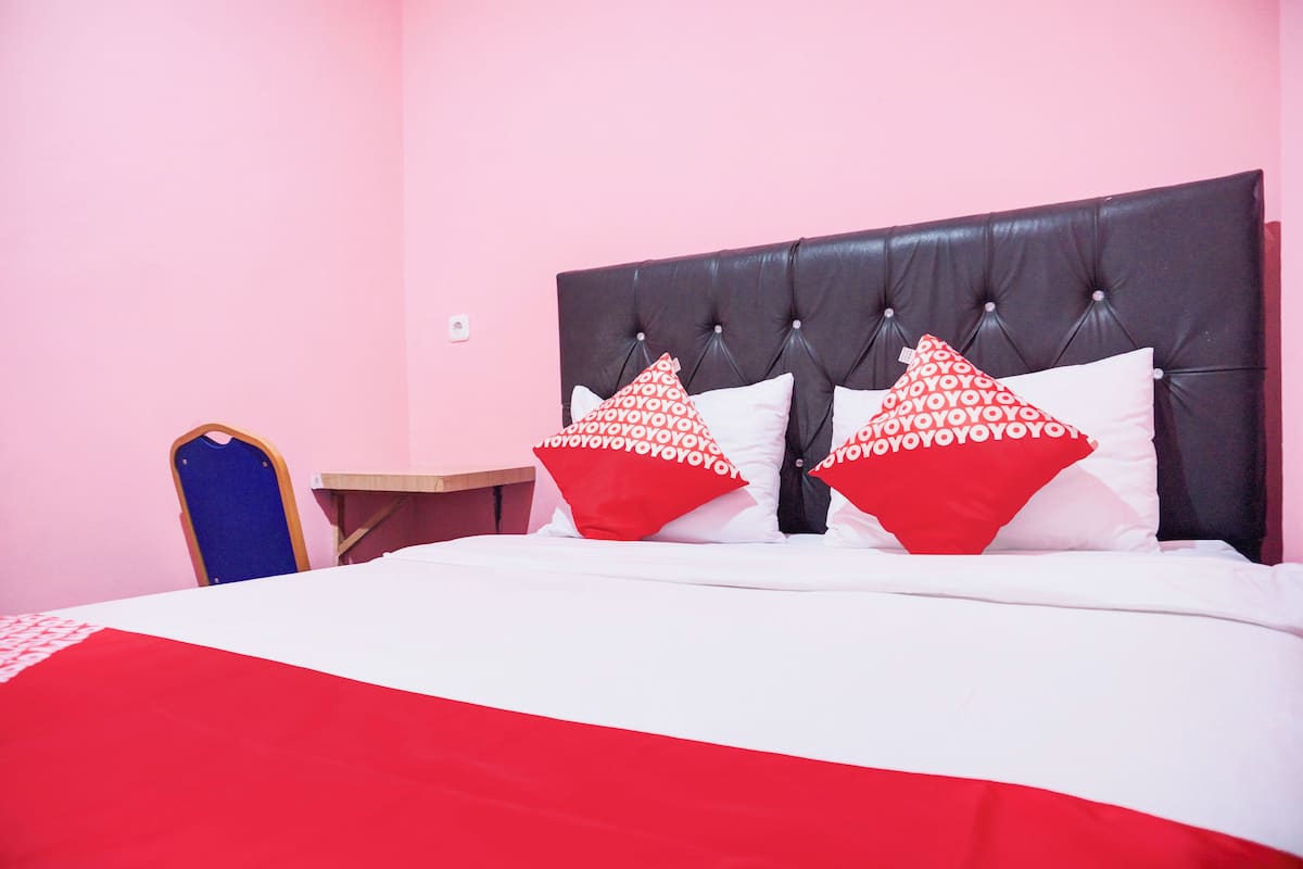 A bed with a red and white bedspread, a dark headboard, and two red pillows with white text.