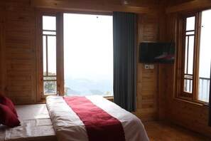 A wooden cabin room with a bed, a television mounted on the wall, and a view of the mountains through the window. - The OutHouse Forest View - Kalatop (Dalhousie)