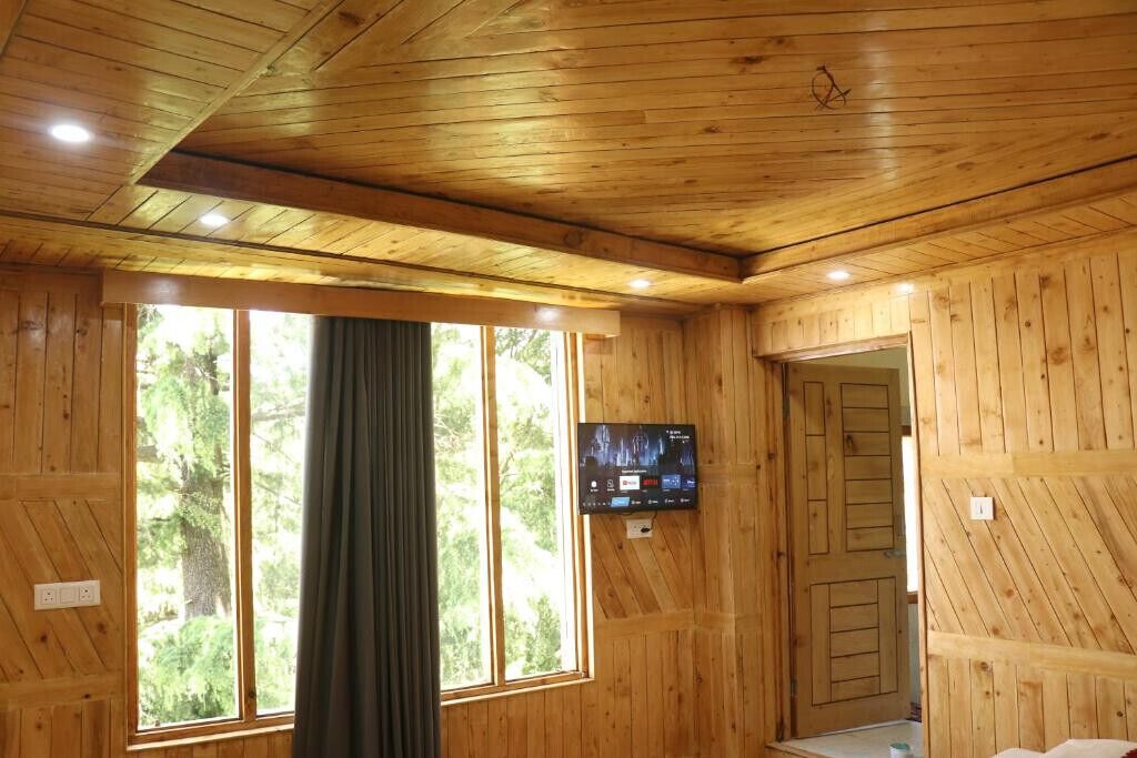A wooden-paneled room with a large window, a television mounted on the wall, and a door leading to another room.