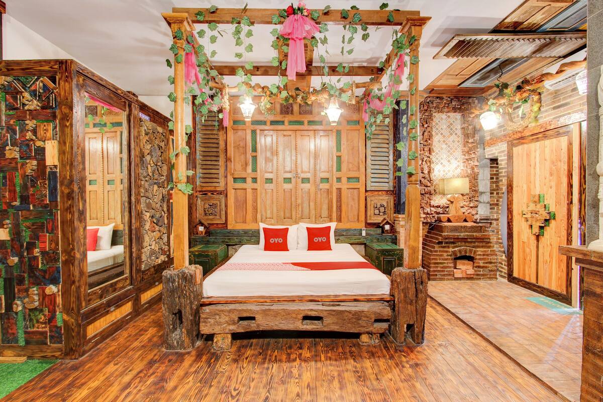 A rustic bedroom with a wooden four-poster bed, a stone fireplace, and a wooden bench.