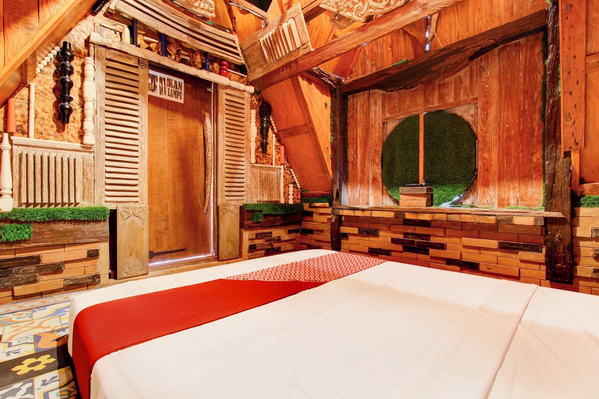 A wooden room with a bed, a window with a circular view, and a wooden door.