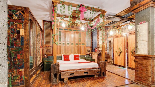 Un dormitorio tradicional de madera con una cama con dosel, un pilar de piedra con rostro tallado y un armario de madera.