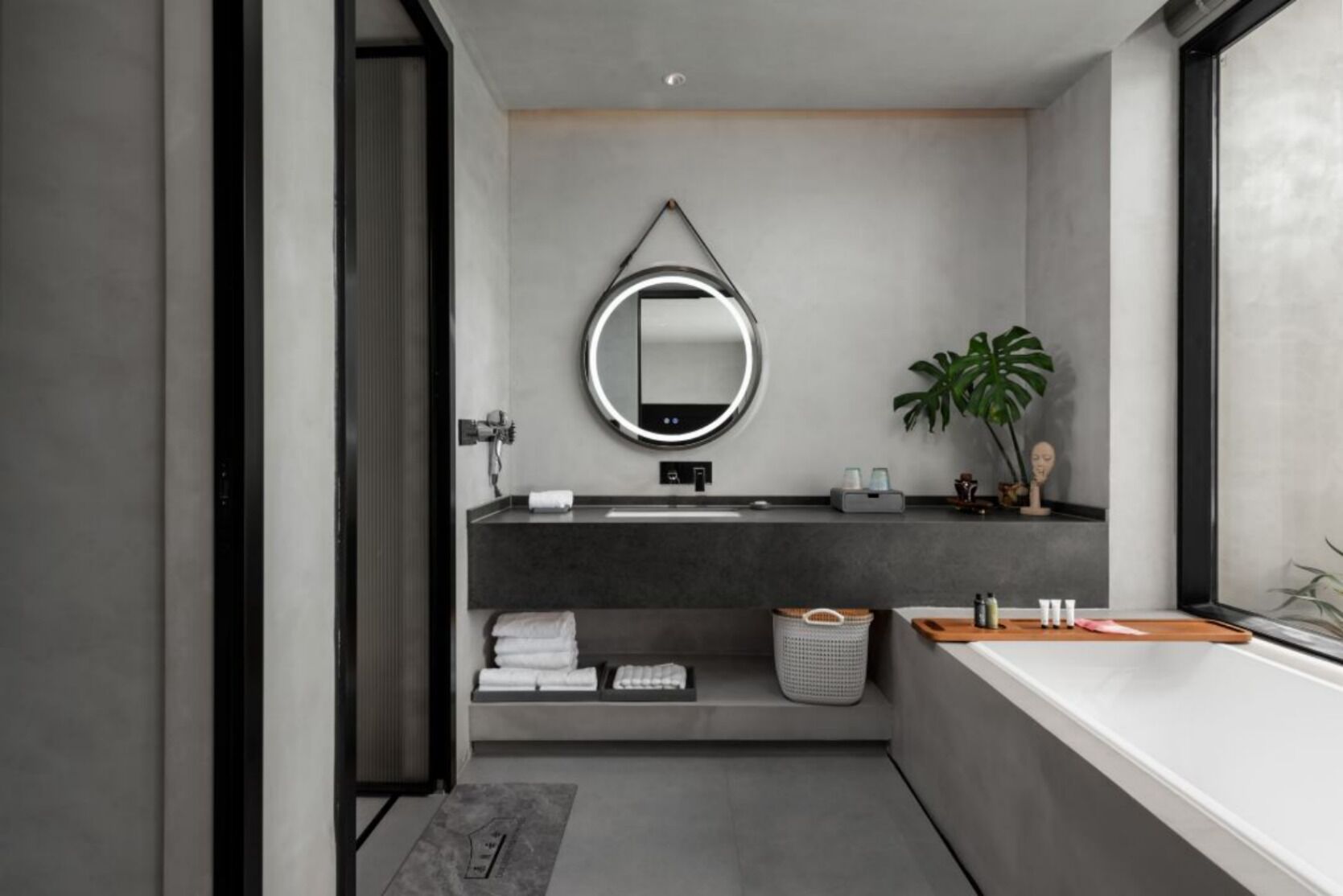 A modern bathroom with a large mirror, a sink, and a plant.