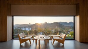 A modern room with a large window, two wicker chairs, and a round table. - HUANG GUO SHU DUO BEI YUN SHE HOTEL (Anshun)